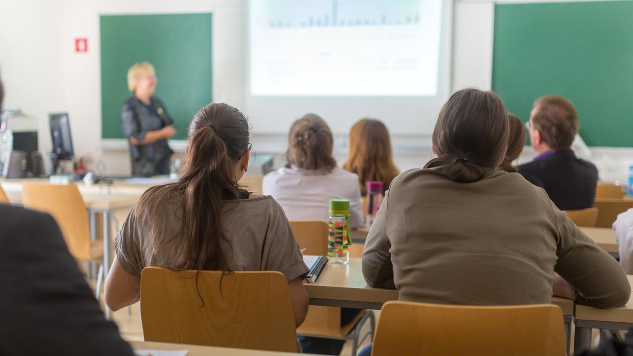 F&ouml;rel&auml;sningssal p&aring; universitet med studenter i f&ouml;rgrunden och en l&auml;rare vid tavlan.
