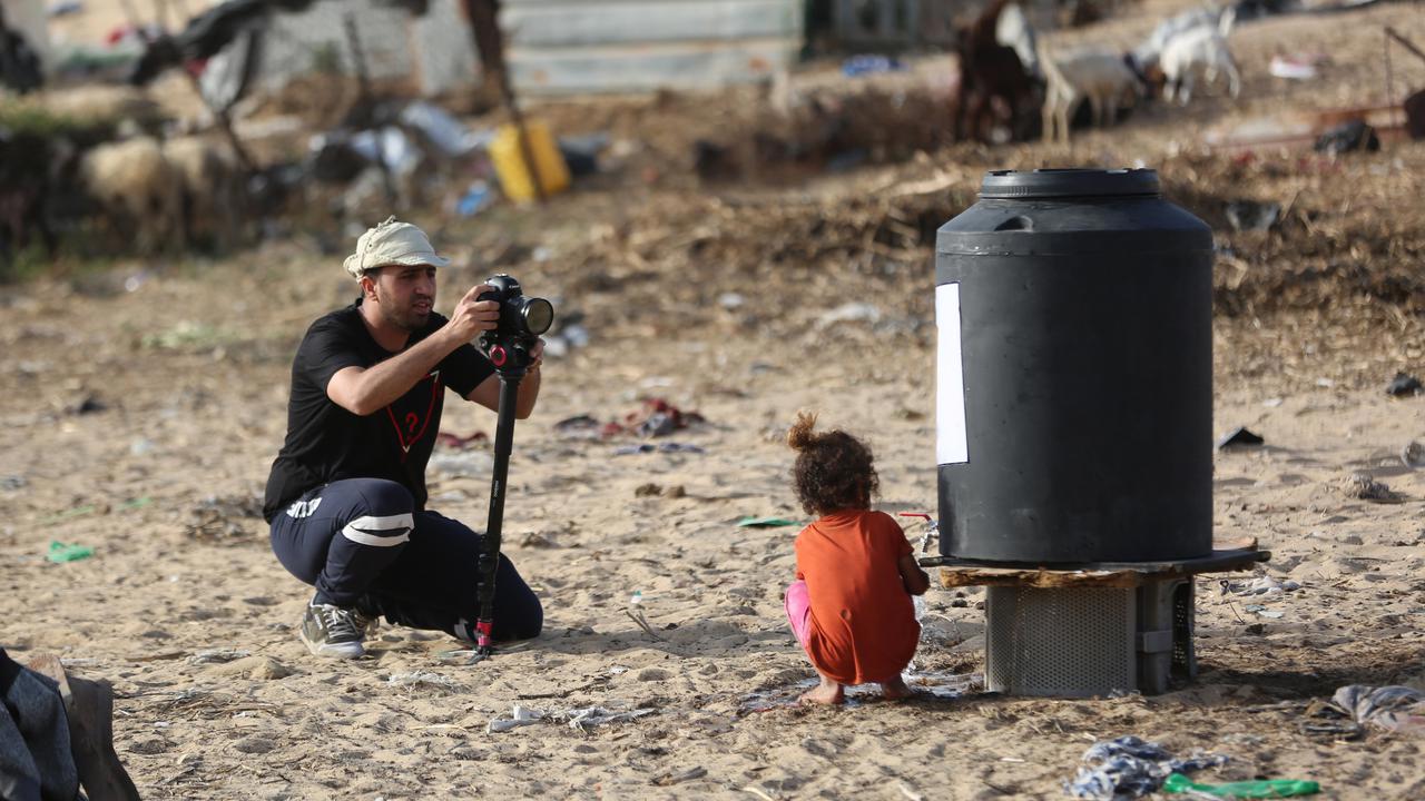 En man som fotograferar en liten flicka p&aring; stranden.