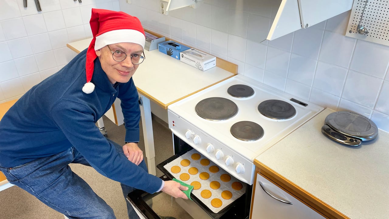 En man i tomteluva tar ut en pl&aring;t pepparkakor ur en ugn