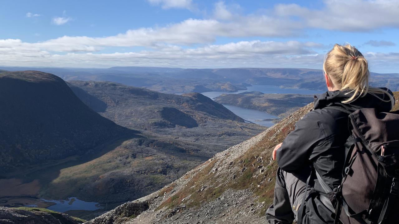 En vandrare med stor ryggs&auml;ck sitter p&aring; en h&ouml;jd, med ryggen v&auml;nd mot kameran och blickar ut &ouml;ver landskapet.