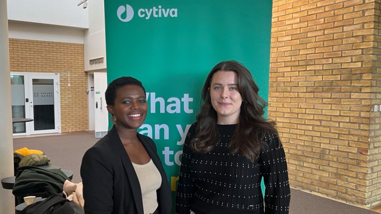 Tv&aring; glada kvinnor st&aring;r framf&ouml;r en gr&ouml;n rollup med Cytivas logotyp.
