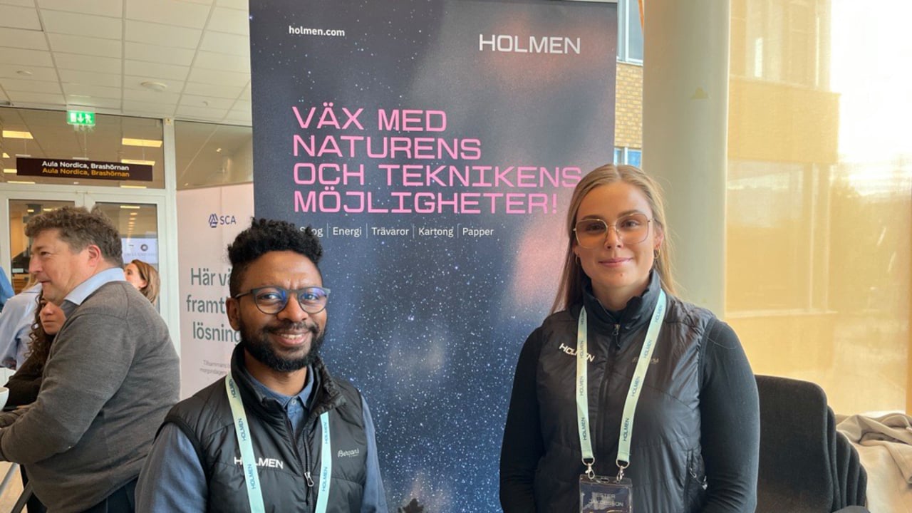 En man och en kvinna st&aring;r tillsammans framf&ouml;r en rollup med Holmen Skogs logotyp.