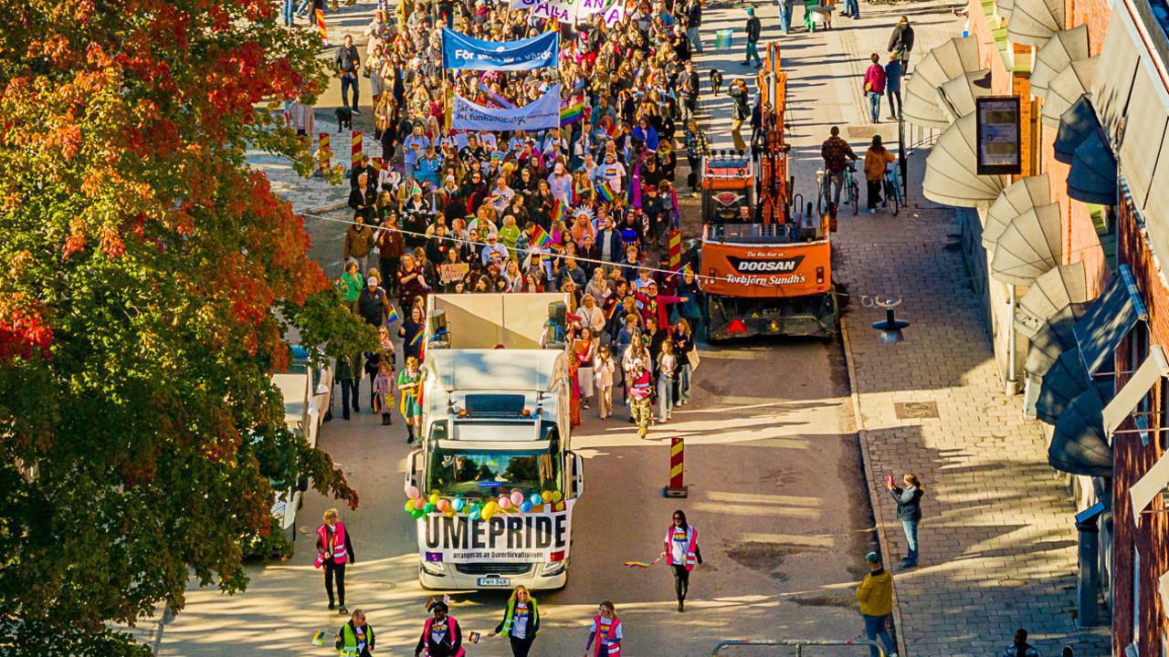Dr&ouml;narbild av en parad av m&auml;nniskor som g&aring;r i Pride-t&aring;get i Ume&aring; 2024, med regnb&aring;gsflaggor och banderoller.