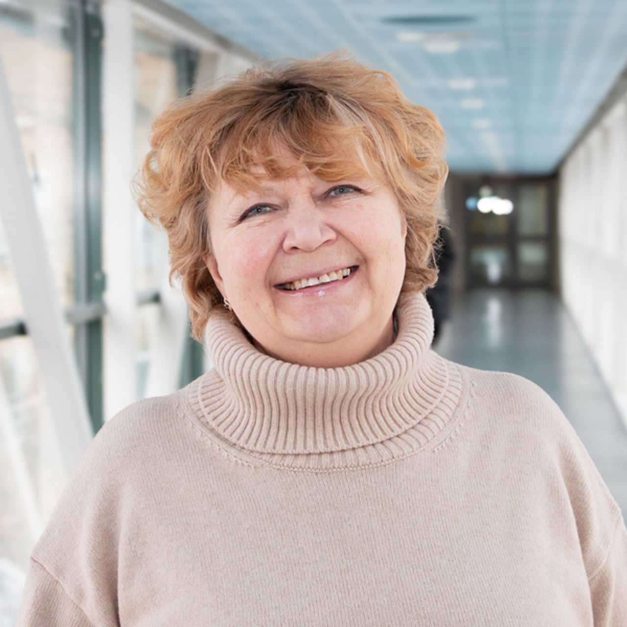 Professor Nina Khairova i en ljus korridor, ikl&auml;dd en beige tr&ouml;ja. Hennes h&aring;r &auml;r blont och kort och hon ler.