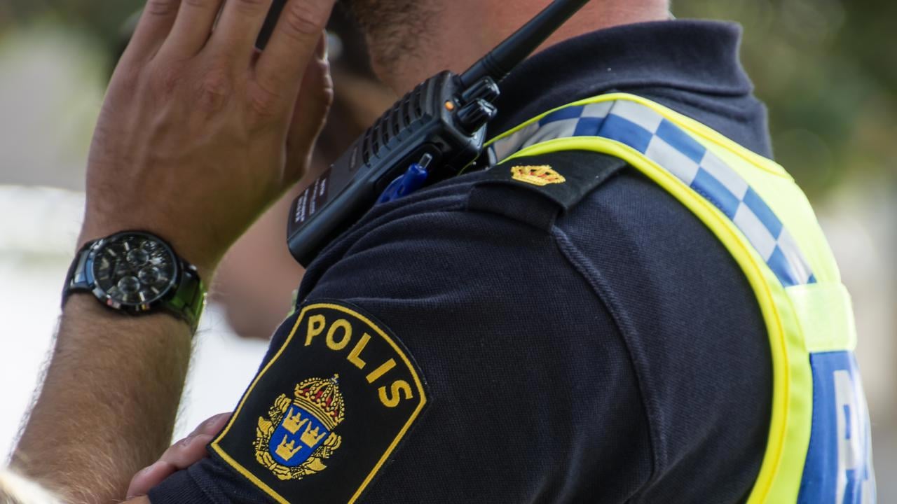 Detalj polis med uniform som pratar i mobil. Man ser arm och tröja med polisens emblem.