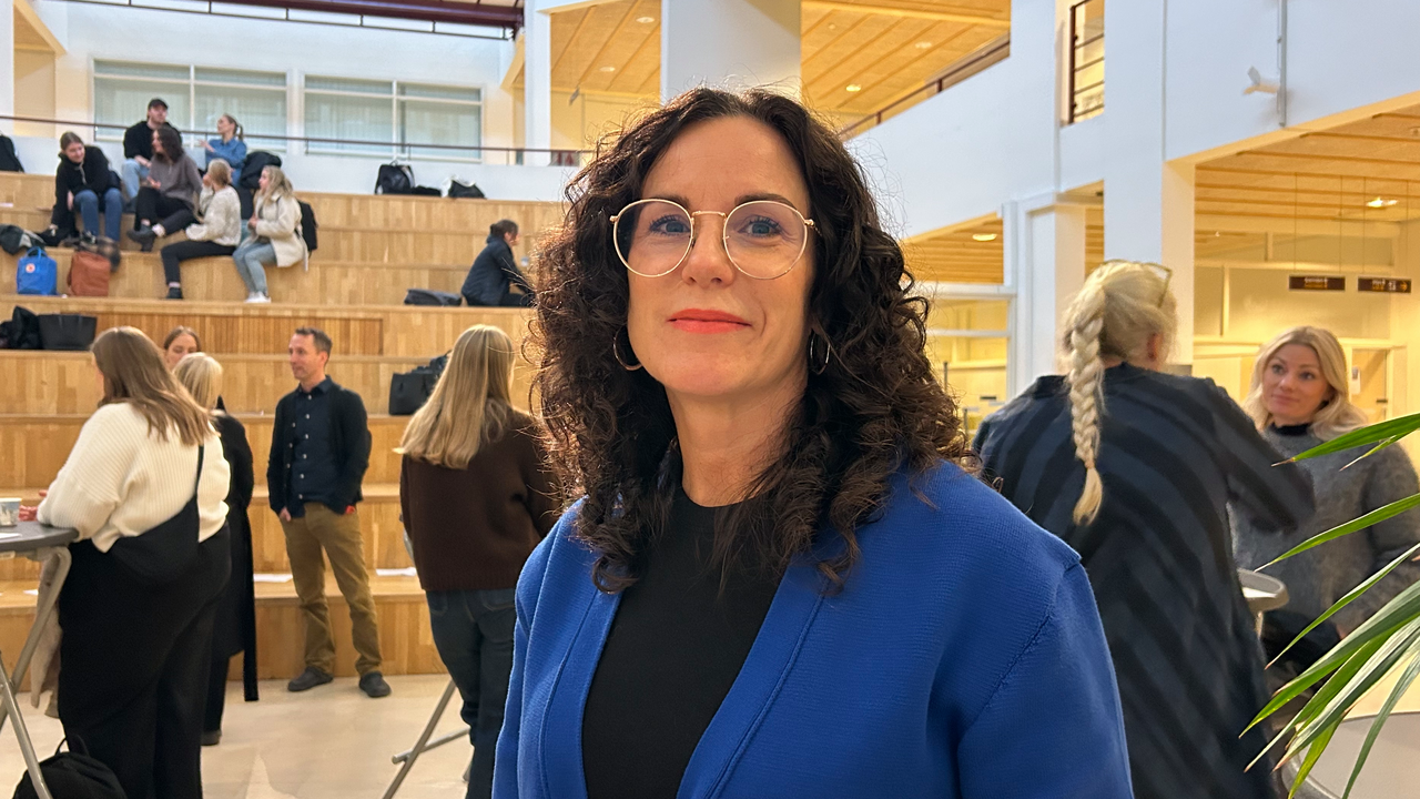 Kvinna i bl&aring; kavaj poserar framf&ouml;r minglande l&auml;rare och studenter.