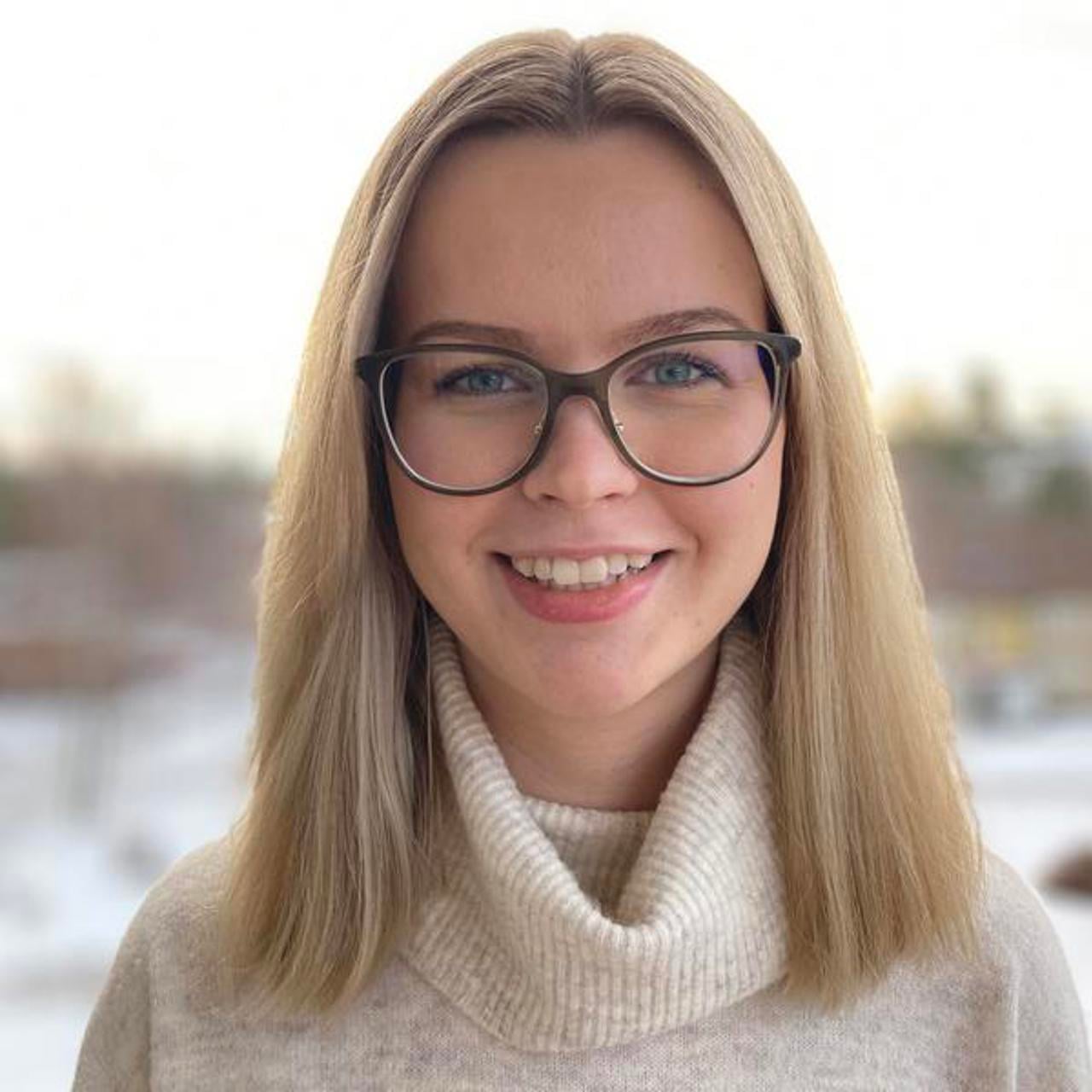 En kvinna med glas&ouml;gon som st&aring;r framf&ouml;r ett f&ouml;nster.