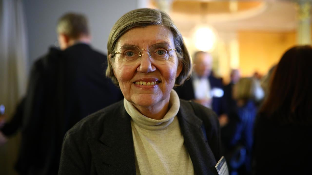 En kvinna med glas&ouml;gon st&aring;r framf&ouml;r en grupp m&auml;nniskor.