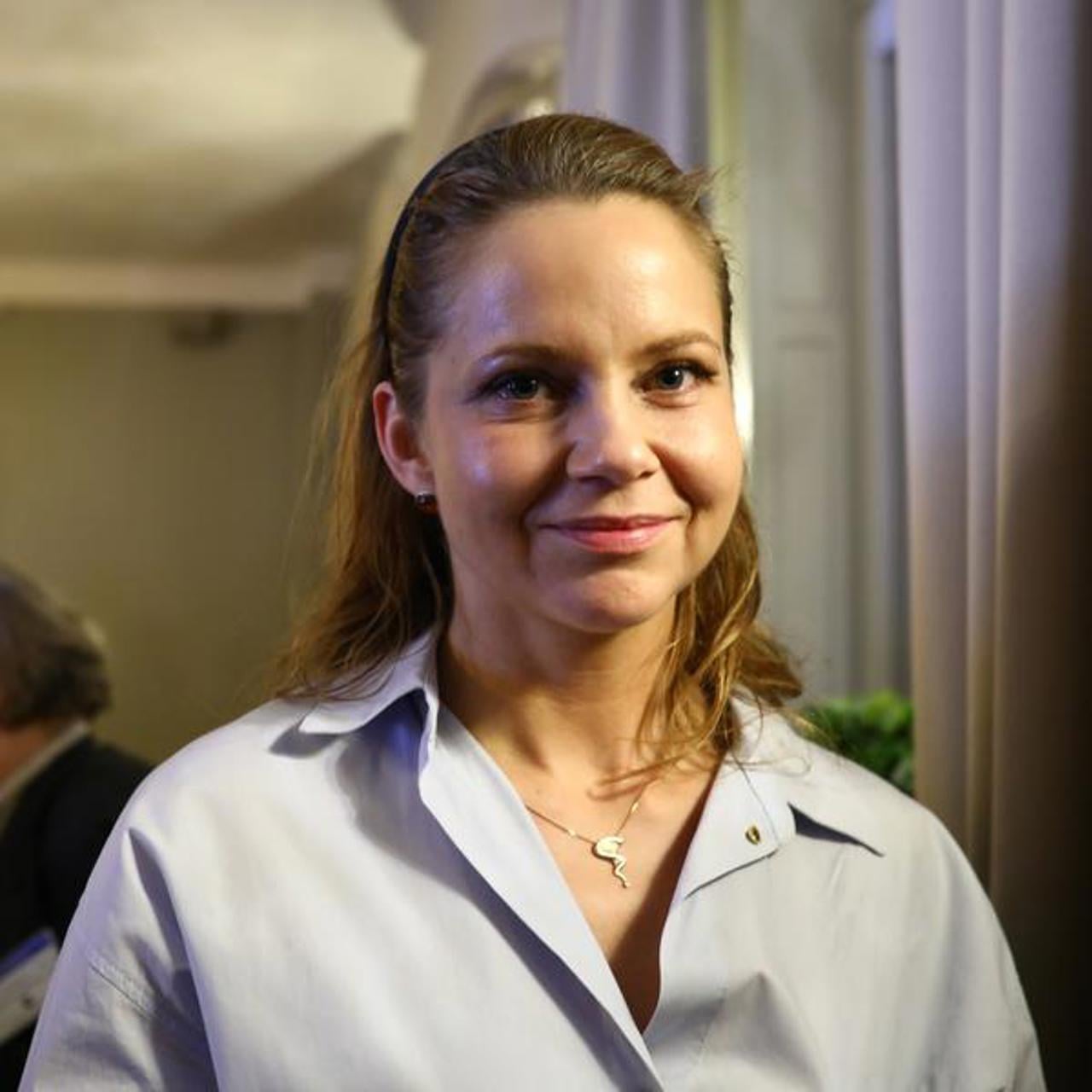 En kvinna som st&aring;r i ett rum med m&auml;nniskor i bakgrunden.