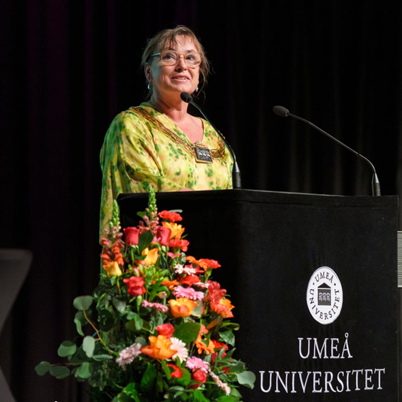 En kvinna st&aring;r p&aring; ett podium framf&ouml;r en mikrofon.