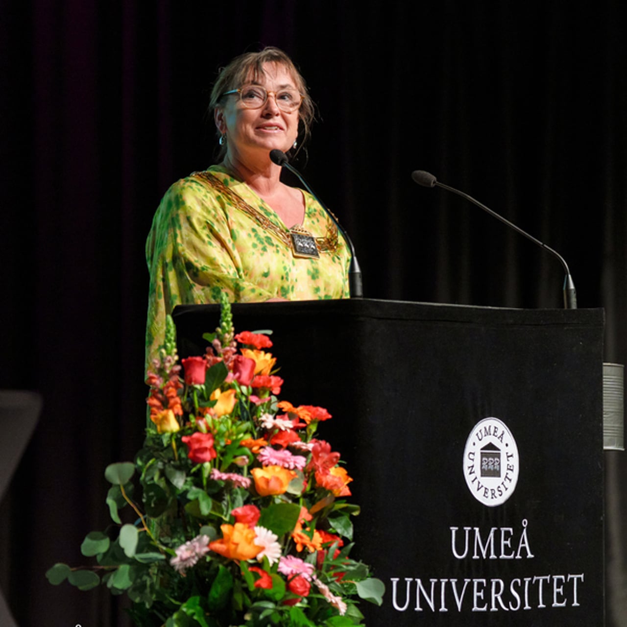 En kvinna st&aring;r p&aring; ett podium framf&ouml;r en mikrofon.
