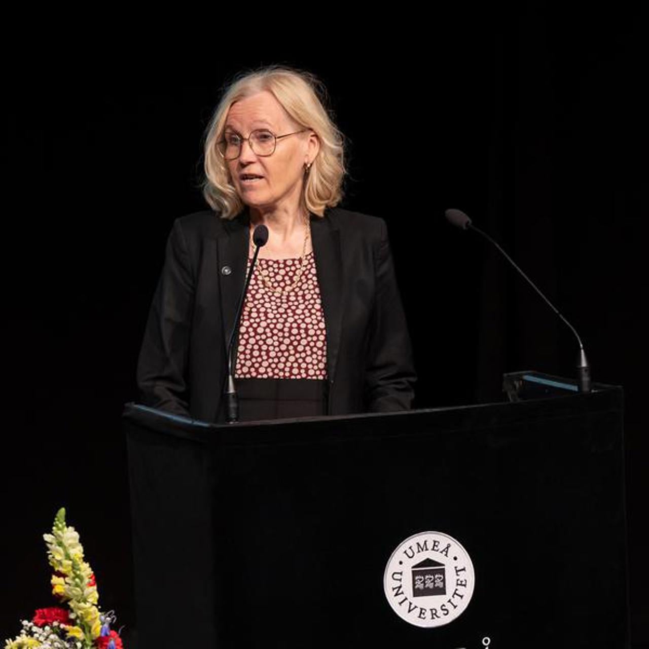En kvinna st&aring;r p&aring; ett podium framf&ouml;r en mikrofon.