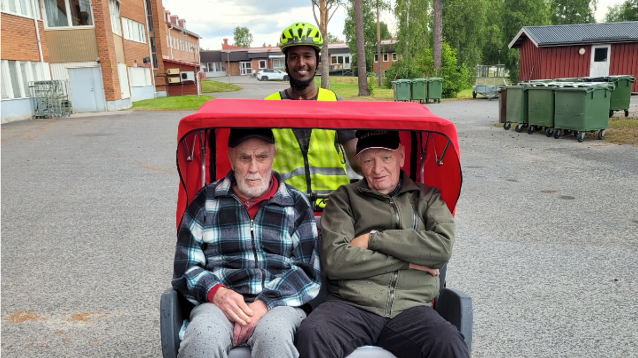 Tv&aring; &auml;ldre m&auml;n blir skjutsade p&aring; elcykel av leende ung man.