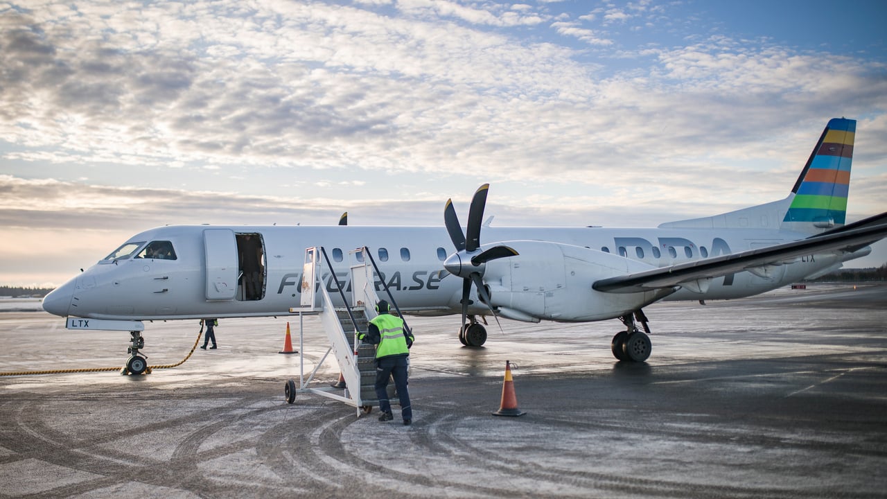 Ett flygplan som st&aring;r p&aring; landningsplattan p&aring; Ume&aring; flygplats. En flygplatsanst&auml;lld h&aring;ller p&aring; att ansluta trappan f&ouml;r att passagerare ska kunna g&aring; ur planet.