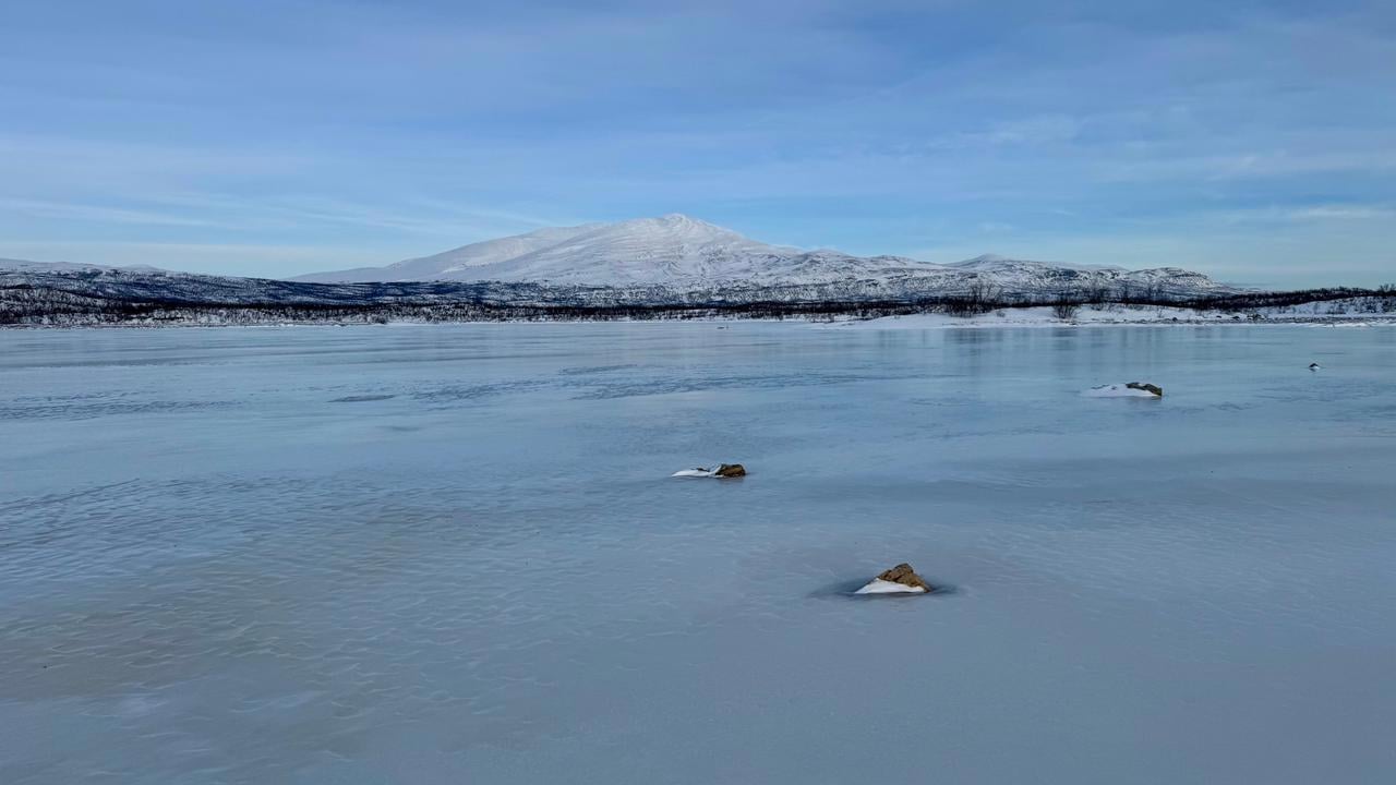 Ett fruset vattendrag med ett fjäll i bakgrunden.