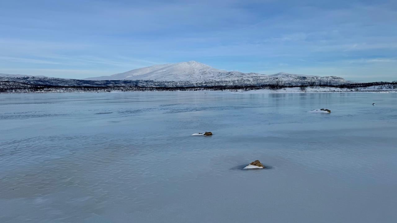 Ett fruset vattendrag med ett fj&auml;ll i bakgrunden.