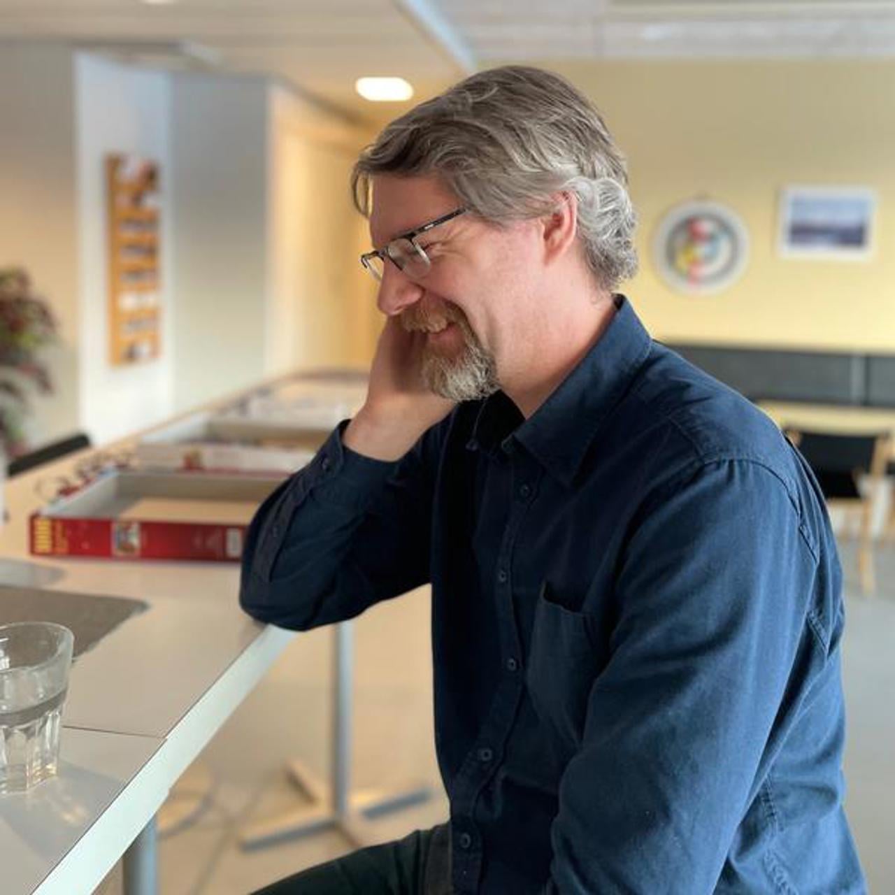 En man sitter vid ett bord och pratar i mobiltelefon.