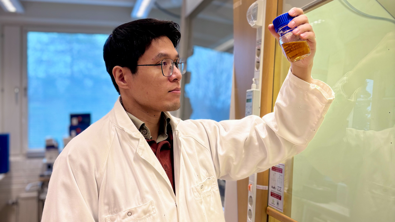 Bild p&aring; doktoranden Van Minh Dinh i vit labbrock st&aring;ende intill ett dragsk&aring;p, h&aring;ller ett preparat i v&auml;nstra handen.