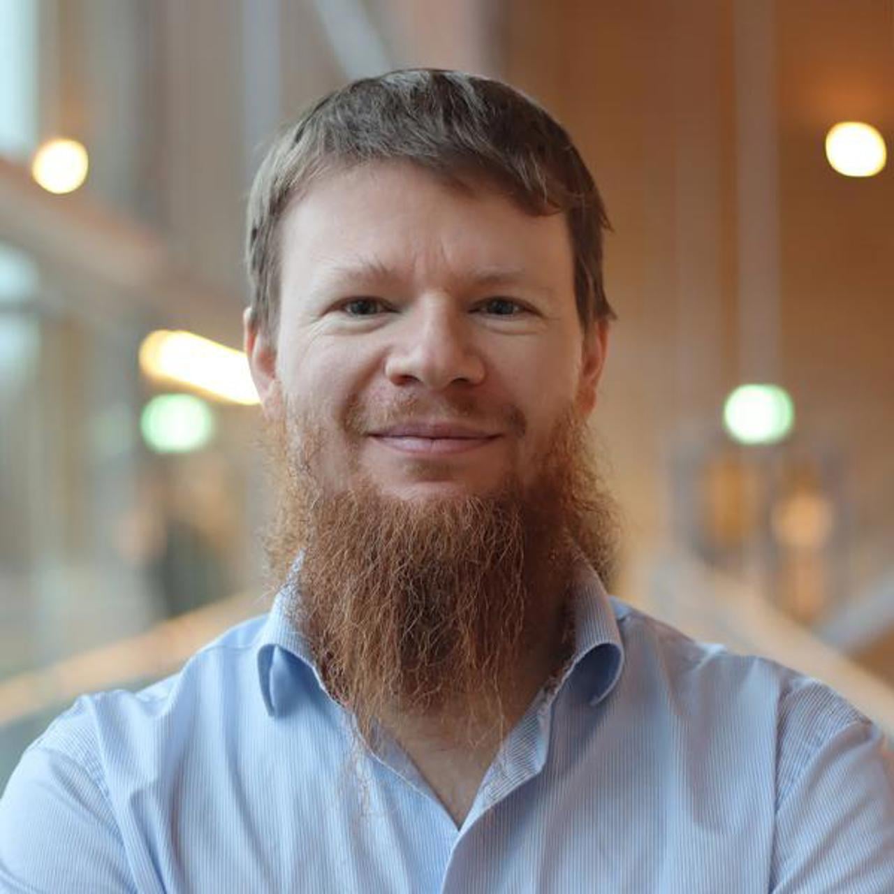 Alexandre Bartel i kort hår och skägg, står vid fönstret i ljusblå skjorta