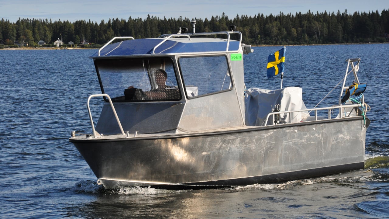 En b&aring;t av metall med stor hytt i f&ouml;ren och flagga i aktern