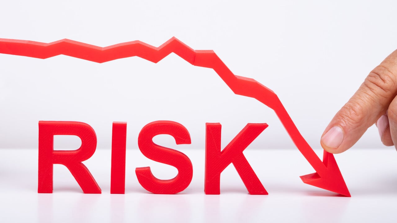 Finger som h&aring;ller p&aring; en ned&aring;tg&aring;ende pil med ordet Risk under. Ska illustrera att minska risken.