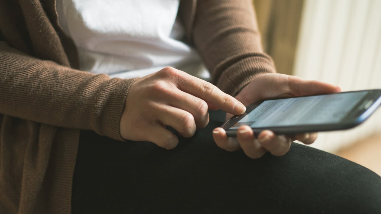 Detalj p&aring; person vars h&auml;nder h&aring;ller i en mobiltelefon som hen surfar p&aring;.