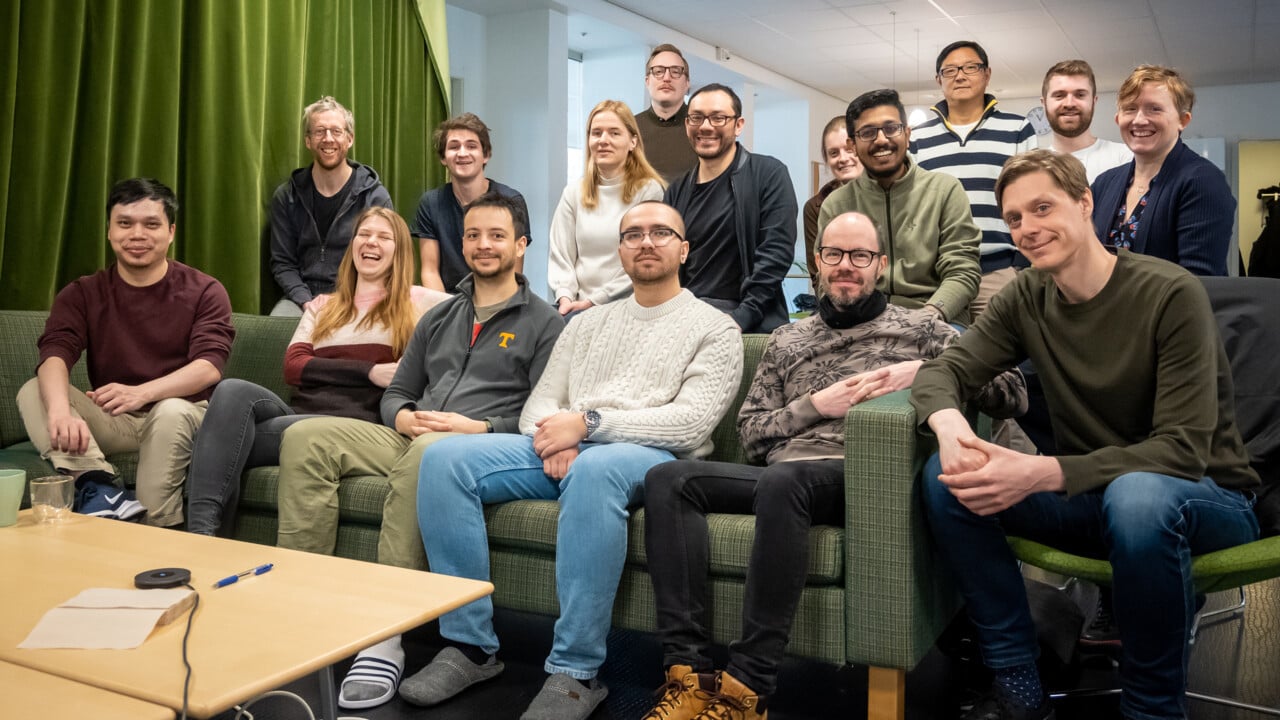 Gruppbild p&aring; ett 15-tal glada personer inomhus.