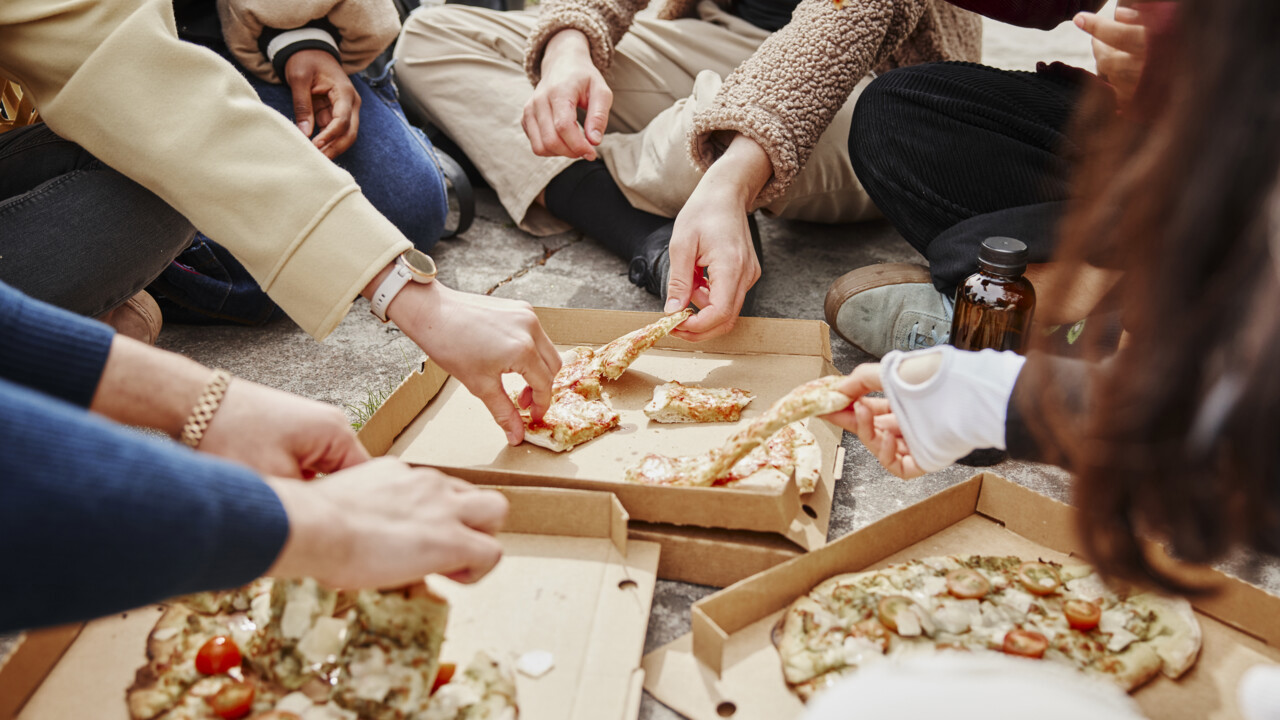 N&auml;rbild p&aring; h&auml;nder som str&auml;cker sig efter pizza.