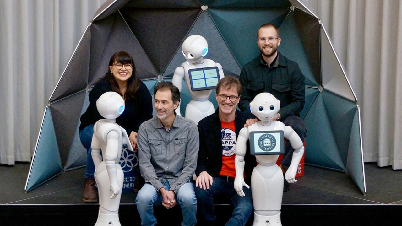 Suna Bensch, universitetslektor i datavetenskap, Filip Edstr&ouml;m, doktorand p&aring; Handelsh&ouml;gskolan, Xavier de Luna, professor vid Handelsh&ouml;gskolan, och Thomas Hellstr&ouml;m, professor i robotik, sitter med tre robotar som tittar p&aring; dem.
