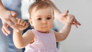 Liten flicka lär sig gå med hjälp av sin mamma.