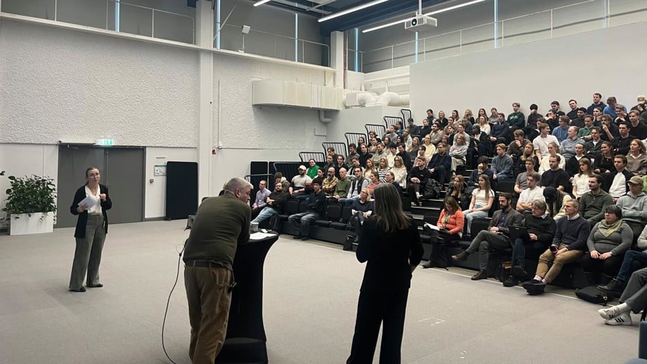 Three people are standing in front of a sitting audience an big room.