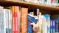 Yngre man väljer ut en bok ur bokhyllan på ett bibliotek.