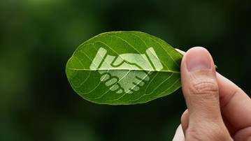 Hand of human is holding painted green leaf with handshake icon, environment social and governance or ESG, Cooperation of organization for prevent climate change  sustainable earth.