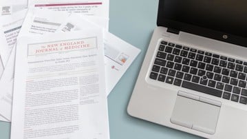 Vetenskapliga artiklar bredvid bärbar dator.