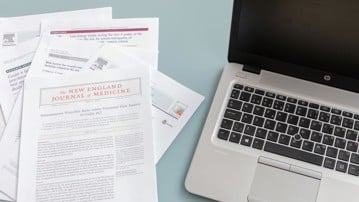 Vetenskapliga artiklar bredvid bärbar dator.