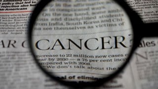 Närbild på ett förstoringsglas som visar ordet Cancer från en tidningstext
