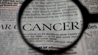 Närbild på ett förstoringsglas som visar ordet Cancer från en tidningstext