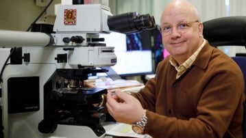 Thomas Brännström, professor och överläkare i patologi samt suppleant i universitetsstyrelsen, vid sitt mikroskop där han tittar på vävnadssnitt som färgats med immunohistokemi.
