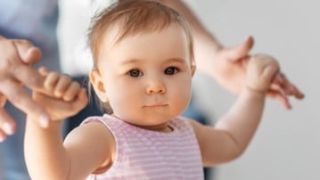 Liten flicka lär sig gå med hjälp av sin mamma.