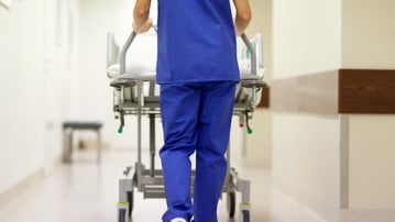 Vårdpersonal skjuter en säng på hjul med patient i en sjukhuskorridor.