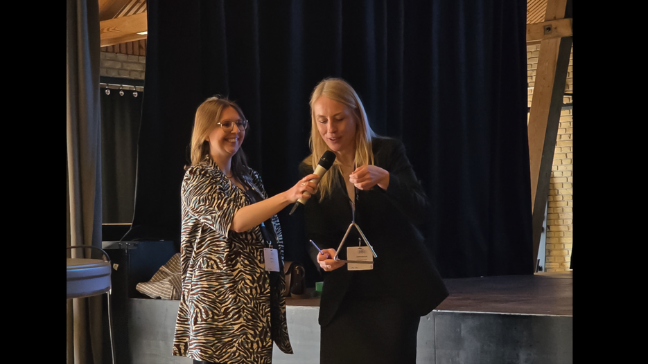 The hosts of DHNB 2026, here represented by Katrine L. Baunvig and Anne Agersnap from Aarhus University. They bring the conference to a close and then hand over the ceremonial triangle to the care of Umeå University.