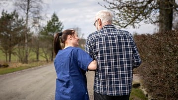 Kvinnlig hemtjänstpersonal hemma hos äldre man och tar promenad