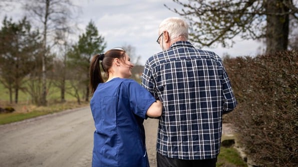 Kvinnlig hemtjänstpersonal hemma hos äldre man och tar promenad