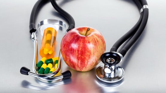 Red apple, medicine capsules and stethoscope on stainless steel table with reflection. Health care concept.
