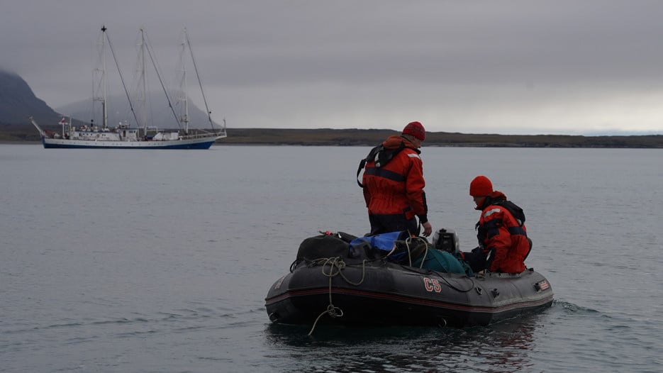 Two people on a small boat, and a bigger boat in the background.