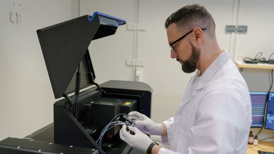Rubén Casanova Sáez wearing a white labcoat, gloves is adding something to a capillary using a pipette.