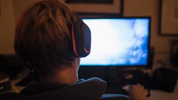 Teenage boy with headphones playing video game in dark bedroom