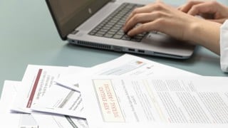 Vetenskapliga artiklar och persons händer som skriver på bärbar dator