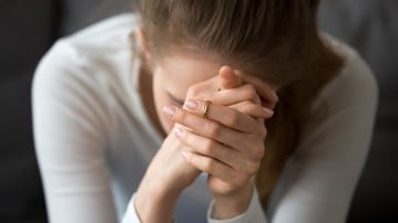 Kvinna som inte mår bra sitter lutad framåt med händerna knäppta framför ansiktet.