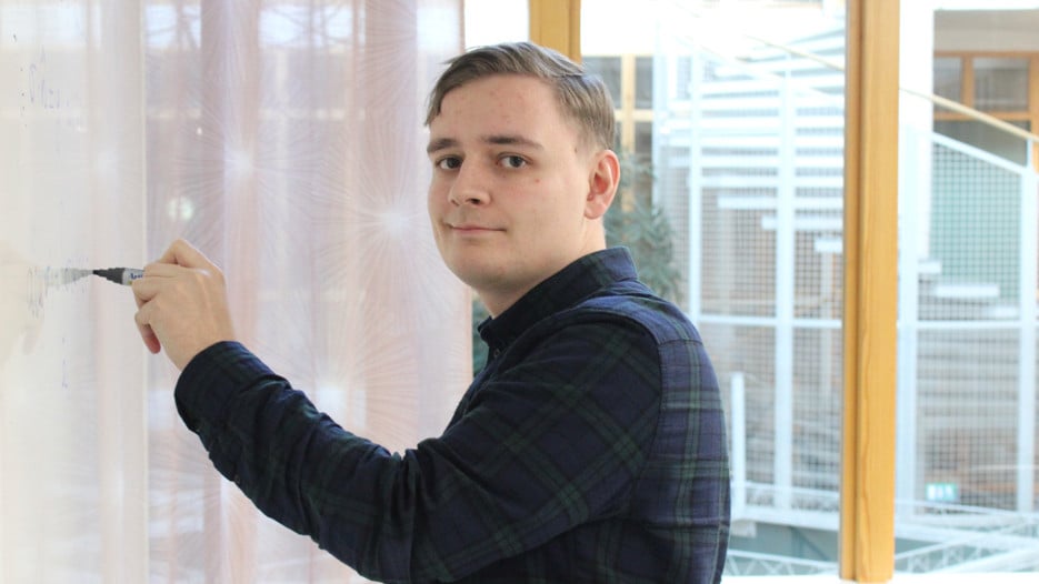 Bilden visar Andreas Granath som skriver på en whiteboardtavlan och tittar in i kameran.